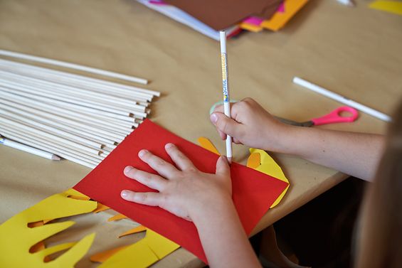 Ein Kind umzeichnet seine Hand mit einem Bleistift auf buntem Papier.